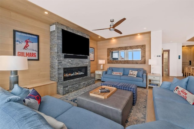 living room with a fireplace, ceiling fan, and wood walls