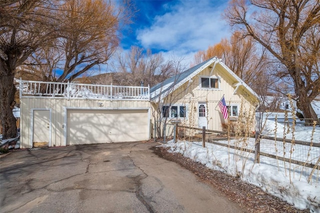 view of front facade with board and batten siding, fence, an attached garage, and aphalt driveway