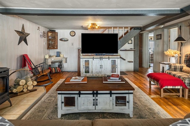 living area with a wood stove, beamed ceiling, and wood finished floors