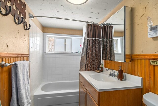 full bath featuring wainscoting, toilet, shower / bath combo with shower curtain, vanity, and wood walls