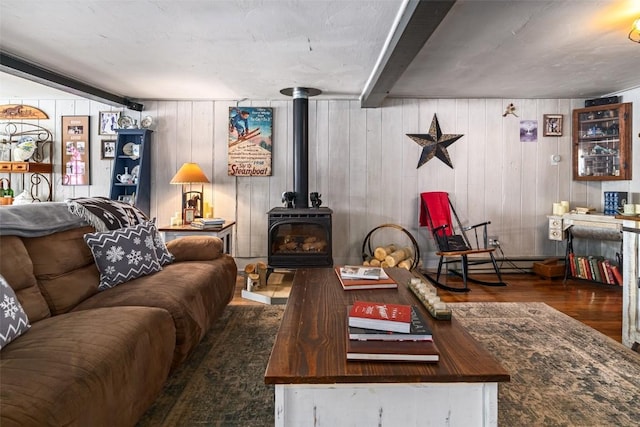 living room featuring a wood stove, baseboard heating, wood finished floors, and beamed ceiling