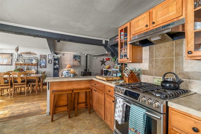 kitchen with tasteful backsplash, glass insert cabinets, gas stove, a peninsula, and under cabinet range hood