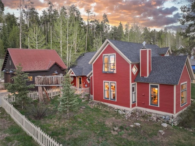 102 S High St, Breckenridge, CO 80424 - back of property at dusk with a chimney, roof with shingles, and view of wooded area