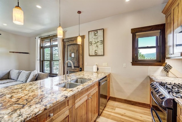 kitchen with stainless steel appliances, a sink, decorative light fixtures, light wood-type flooring, and light stone countertops