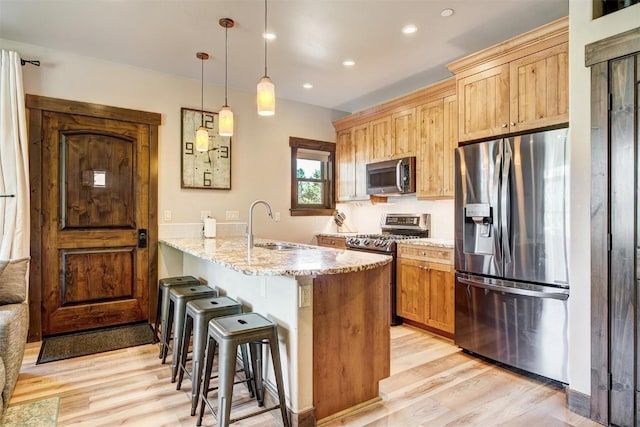 kitchen with a peninsula, light wood-style floors, a kitchen bar, and appliances with stainless steel finishes