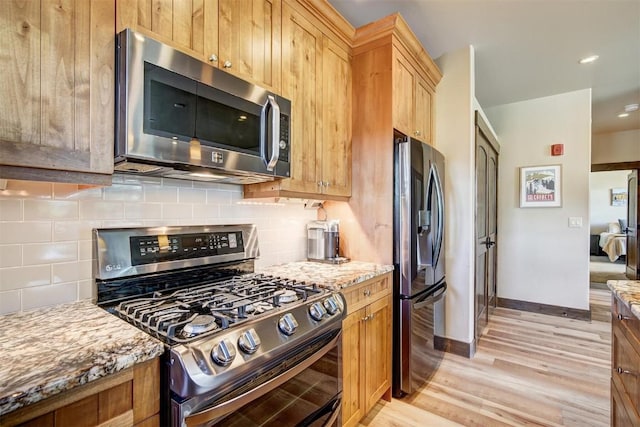 kitchen featuring stainless steel appliances, backsplash, light stone countertops, baseboards, and light wood-style flooring
