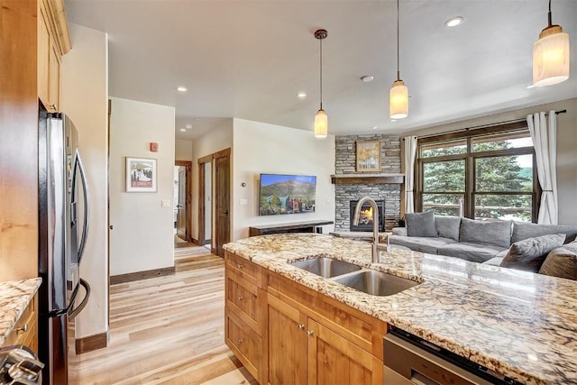 kitchen with a sink, open floor plan, light wood-style floors, a stone fireplace, and appliances with stainless steel finishes