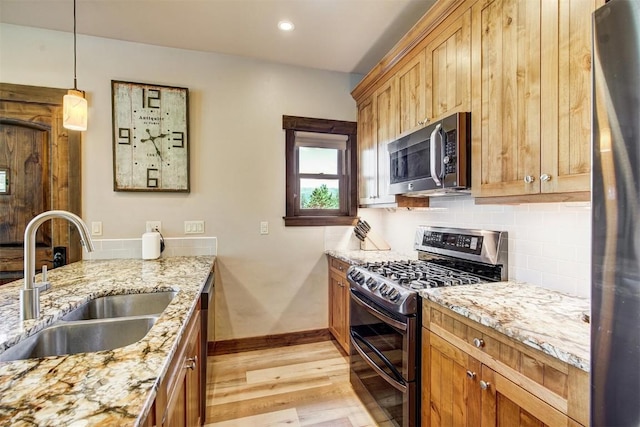 kitchen featuring light wood finished floors, a sink, backsplash, light stone counters, and appliances with stainless steel finishes