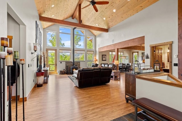 living area featuring a ceiling fan, a wood stove, beam ceiling, wood finished floors, and high vaulted ceiling
