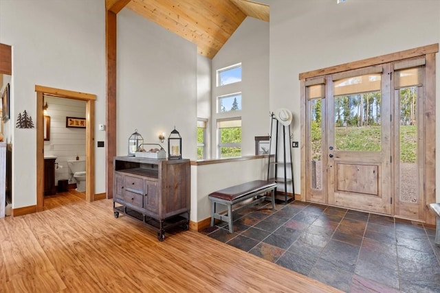 foyer entrance with baseboards, stone tile floors, and high vaulted ceiling