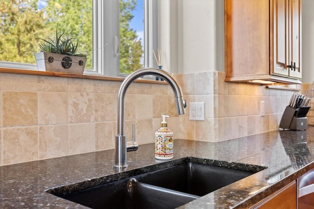 room details with brown cabinetry, a sink, dark stone counters, and tasteful backsplash