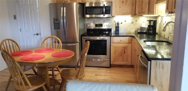 kitchen featuring a sink, appliances with stainless steel finishes, decorative backsplash, and light wood-style floors