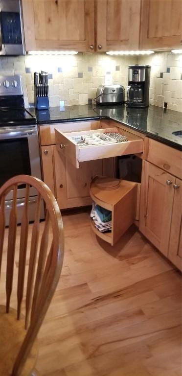kitchen with dark countertops, appliances with stainless steel finishes, tasteful backsplash, and light wood-type flooring