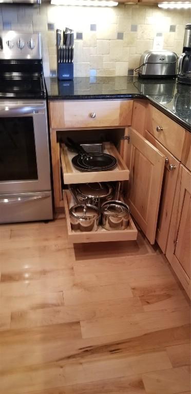 kitchen featuring dark countertops, decorative backsplash, light wood-style flooring, and stainless steel range with electric cooktop