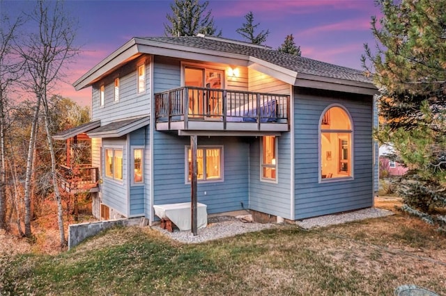 back house at dusk with a balcony and a lawn