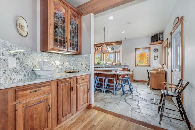 kitchen with decorative light fixtures, light stone counters, light hardwood / wood-style flooring, and tasteful backsplash