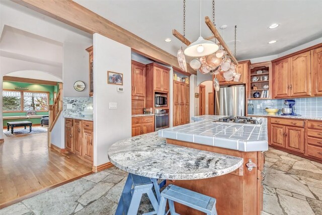 kitchen with stainless steel appliances, billiards, tile countertops, an island with sink, and decorative backsplash