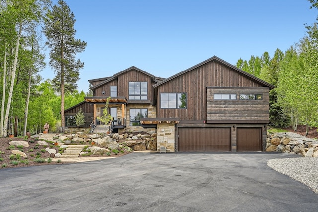 chalet / cabin featuring a garage, stairs, stone siding, and aphalt driveway