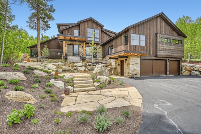 view of front of home with an attached garage, stairs, stone siding, and aphalt driveway