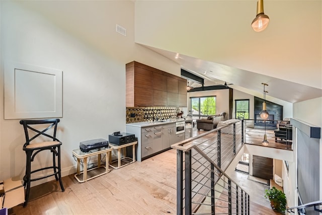 kitchen featuring light wood finished floors, light countertops, lofted ceiling, backsplash, and visible vents