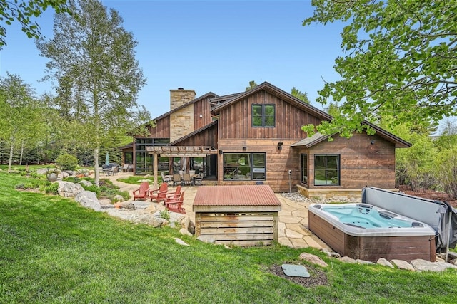 back of house with a lawn, a patio, a chimney, and a hot tub