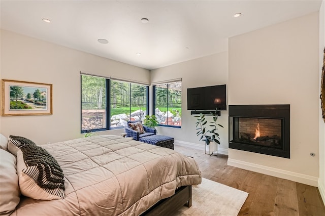 bedroom featuring baseboards, recessed lighting, wood finished floors, and a warm lit fireplace