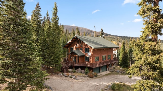 view of side of property with an attached garage, dirt driveway, a forest view, and a deck with mountain view