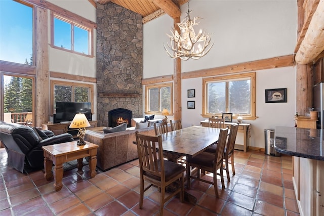 dining room with a notable chandelier, beamed ceiling, wooden ceiling, a stone fireplace, and high vaulted ceiling