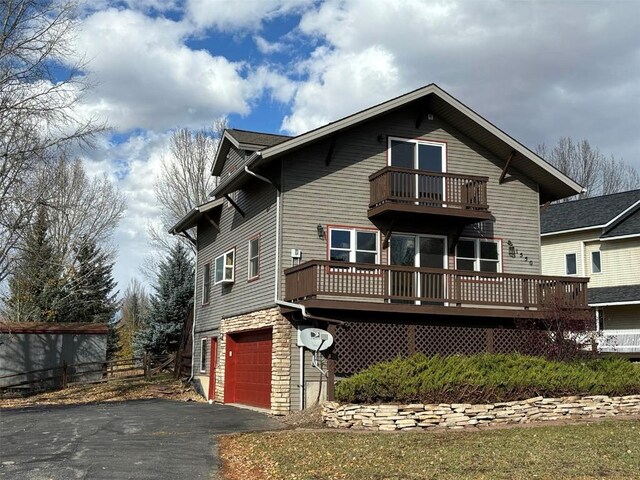 1550 Red Hawk Ct, Steamboat Springs, CO 80487 - view of front facade with a balcony, driveway, stone siding, a deck, and a garage