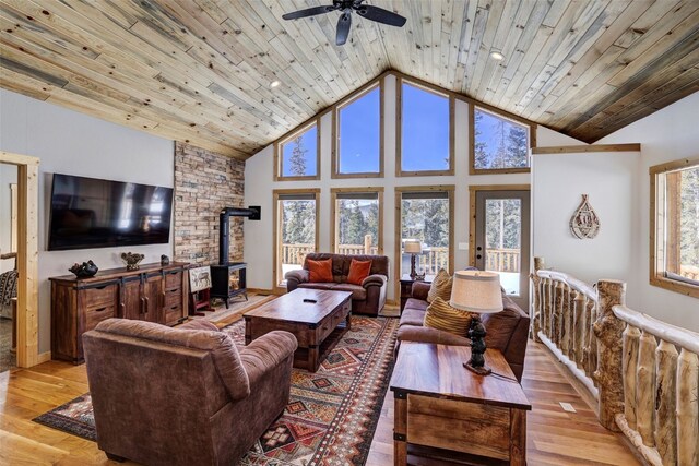 living area featuring a wood stove, a ceiling fan, light wood finished floors, and high vaulted ceiling