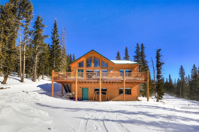snow covered house with faux log siding and a deck