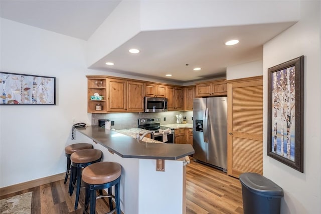 1463 Flattop Cir Unit 302, Steamboat Springs, CO 80487 - kitchen featuring appliances with stainless steel finishes, a peninsula, brown cabinets, a breakfast bar area, and light wood-type flooring