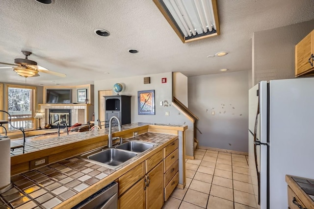kitchen with a ceiling fan, tile counters, a sink, light tile patterned flooring, and freestanding refrigerator