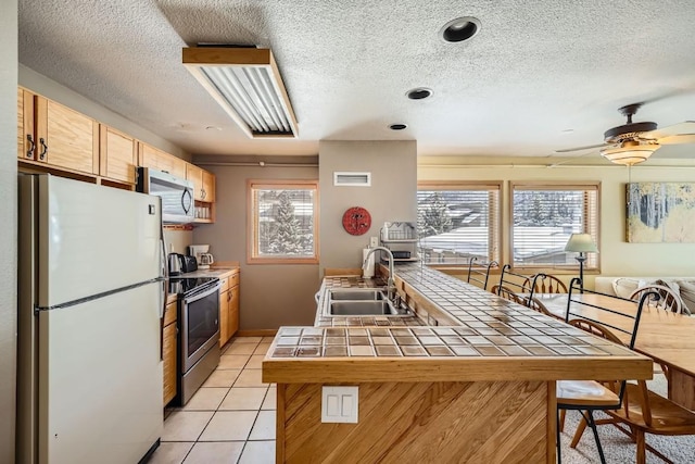 kitchen with appliances with stainless steel finishes, tile counters, a sink, and a textured ceiling