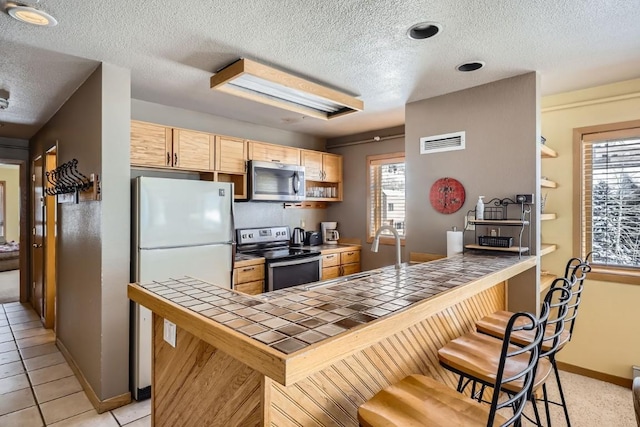 kitchen featuring tile counters, a textured ceiling, a peninsula, appliances with stainless steel finishes, and visible vents