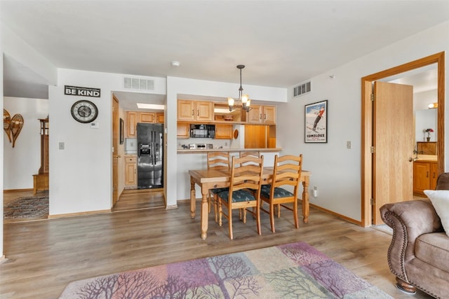 dining area featuring light wood finished floors, baseboards, visible vents, and an inviting chandelier