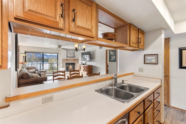 kitchen with light wood-style flooring, a sink, ceiling fan, light countertops, and a fireplace