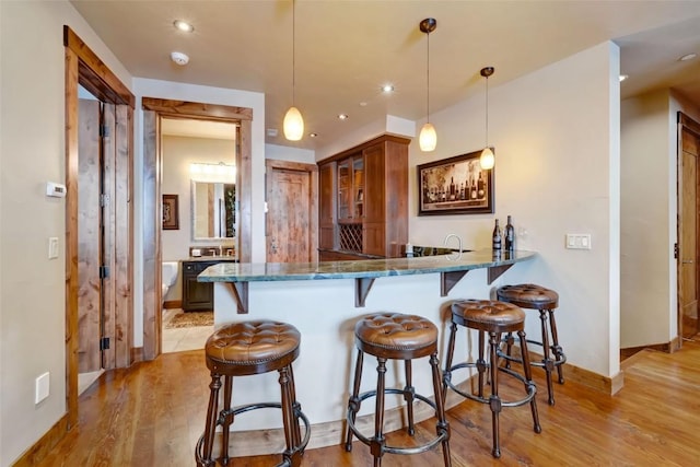 2542 Ski Trail Ln, Steamboat Springs, CO 80487 - kitchen featuring glass insert cabinets, light wood-style flooring, dark stone counters, a breakfast bar area, and brown cabinetry