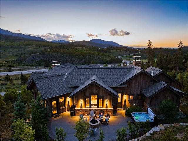 455 Highfield Trl, Breckenridge, CO 80424 - back of house at dusk with a shingled roof, a patio area, a mountain view, a chimney, and stone siding
