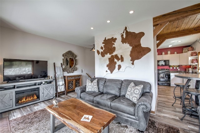 living room with recessed lighting, a glass covered fireplace, light wood-style flooring, and beam ceiling