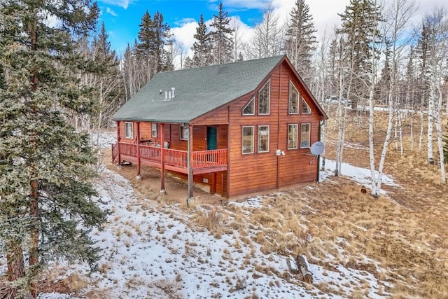 snow covered rear of property featuring a wooden deck and roof with shingles
