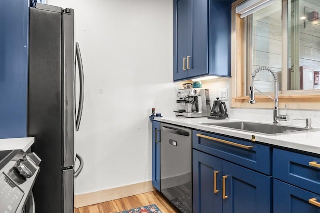kitchen featuring a sink, blue cabinetry, appliances with stainless steel finishes, light wood finished floors, and light countertops