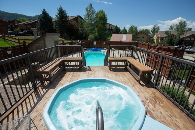 view of swimming pool featuring a wooden deck, a hot tub, and a fenced backyard