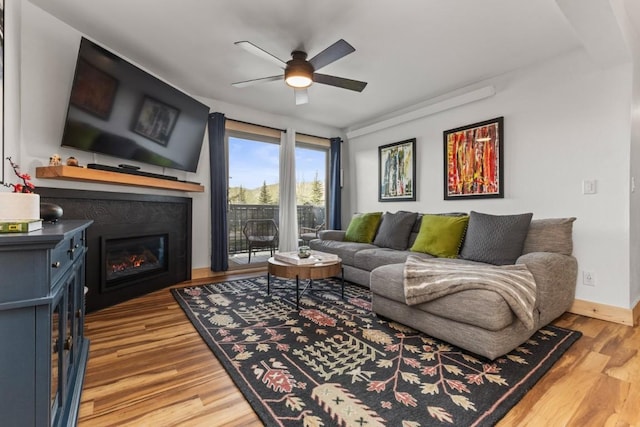 living room with ceiling fan, a glass covered fireplace, wood finished floors, and baseboards