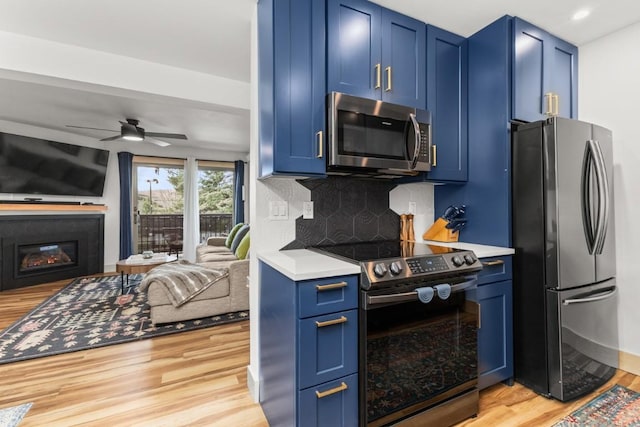 kitchen featuring appliances with stainless steel finishes, blue cabinetry, light wood-type flooring, light countertops, and open floor plan