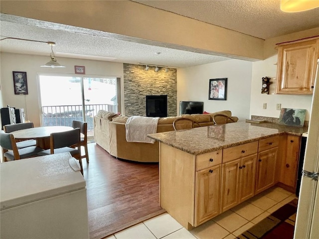 kitchen with a textured ceiling, light tile patterned floors, a fireplace, a peninsula, and light stone countertops