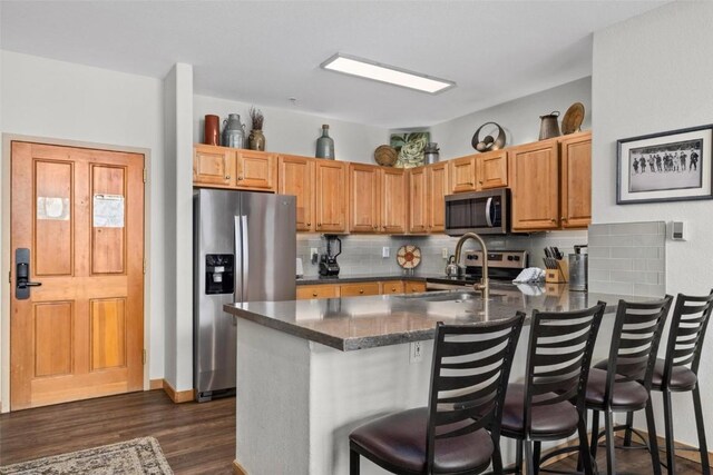 23110 US Highway 6 Unit 5044, Keystone, CO 80435 - kitchen with appliances with stainless steel finishes, a peninsula, backsplash, dark wood-type flooring, and a kitchen bar