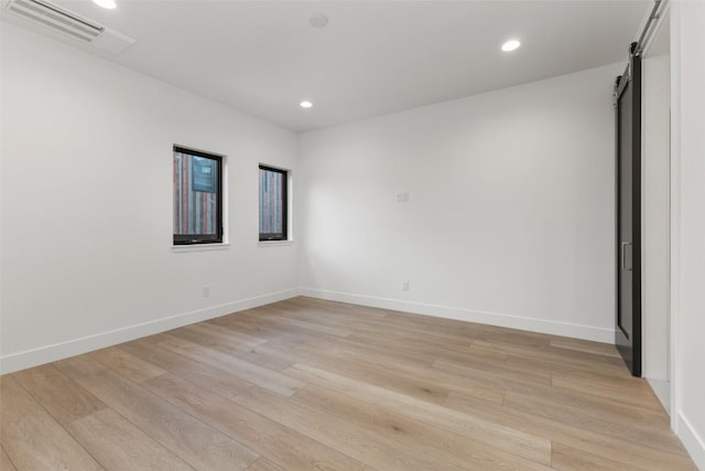 unfurnished room featuring a barn door and light hardwood / wood-style floors