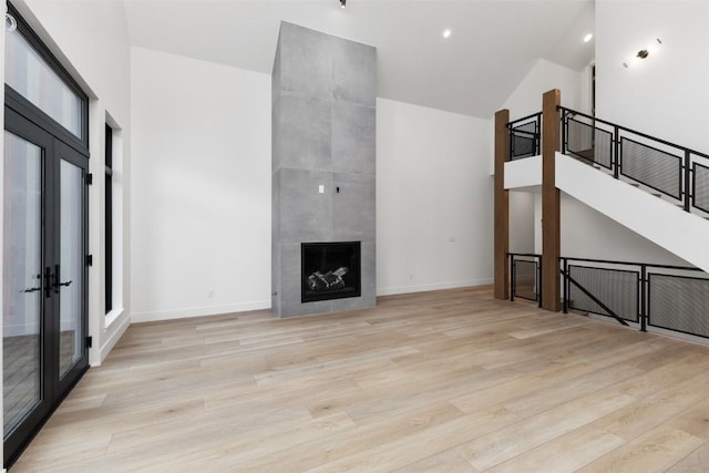 unfurnished living room with a tile fireplace, french doors, light wood-type flooring, and vaulted ceiling