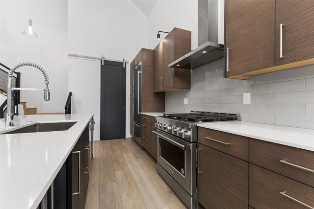 kitchen with sink, stainless steel appliances, wall chimney range hood, a barn door, and decorative light fixtures